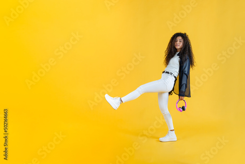 Young woman taking long step while walking in studio shot with yellow background