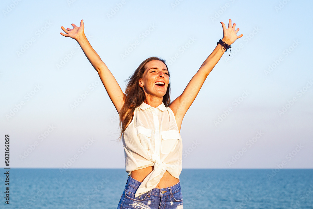 Smiling young woman with raised hands on the background of the sea. Smiling young woman with raised hands on the background of the sea.
