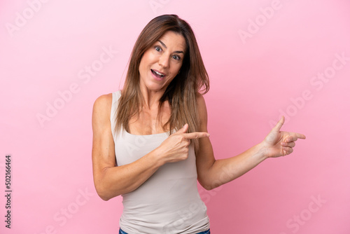 Middle age caucasian woman isolated on pink background surprised and pointing side © luismolinero