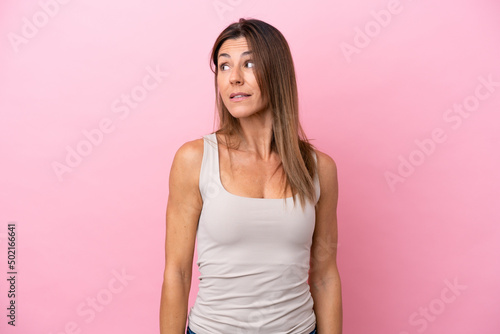 Middle age caucasian woman isolated on pink background making doubts gesture looking side