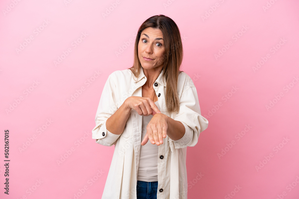 Middle age caucasian woman isolated on pink background making the gesture of being late Middle age caucasian woman isolated on pink background making the gesture of being late