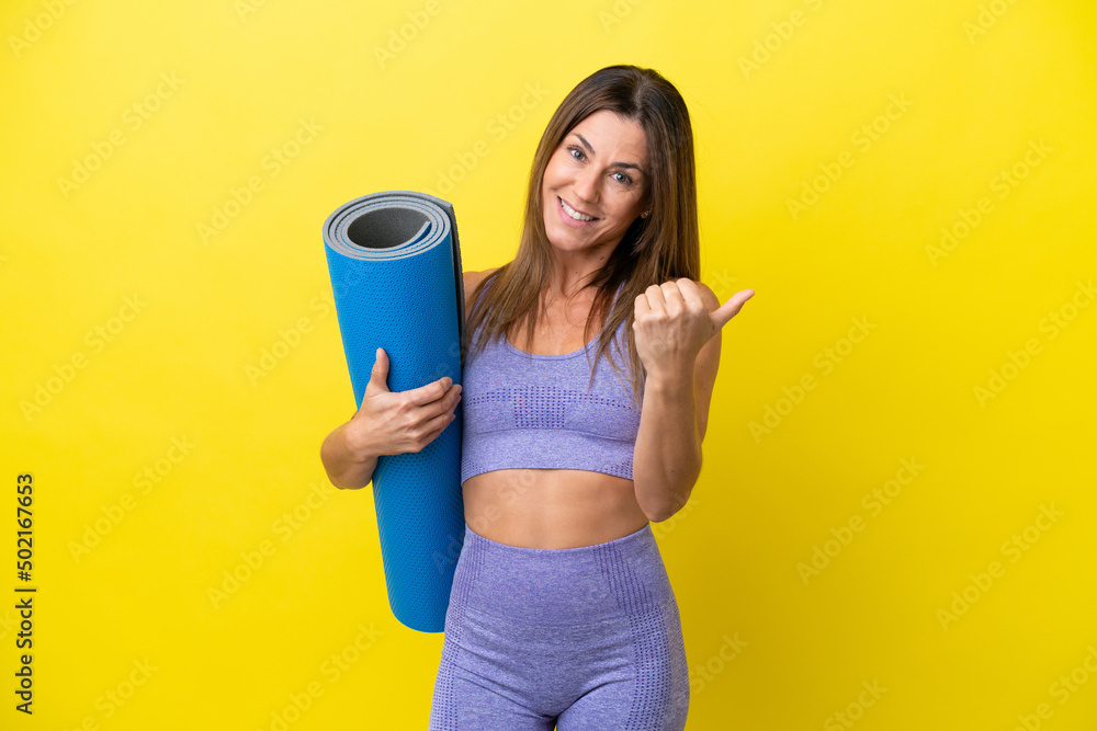 Sport woman going to yoga classes while holding a mat isolated non yellow background inviting to come with hand. Happy that you came Sport woman going to yoga classes while holding a mat isolated non yellow background inviting to come with hand. Happy that you came