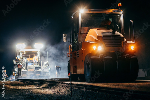 Industrial pavement truck is laying fresh asphalt on construction site at night. Road service repairs the highway 