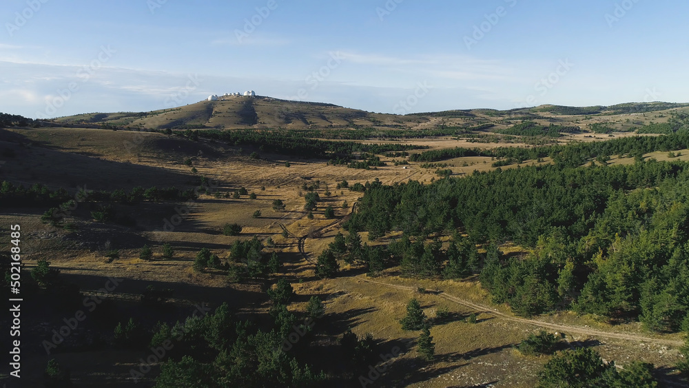 View of panorama from land of hilly valley. Shot. Top view of stone hills and horizon with blue sky. White observatories on horizon