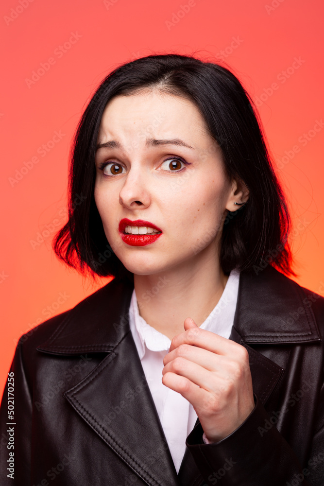 brunette woman with red lipstick on her lips in a black leather jacket and white shirt, red background brunette woman with red lipstick on her lips in a black leather jacket and white shirt, red background