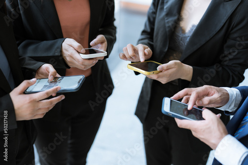 A Group of young businesspeople standing and using smartphones together concepts communication. 