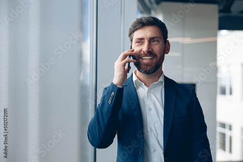 Smiling businessman uses mobile phone to call his business partner while working in the office. 