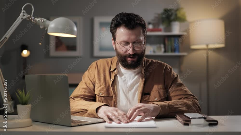 Man looking at camera and speaks. Bearded teacher with glasses in home office is talking on video call. Remote online salesperson makes presentation from apartment Man looking at camera and speaks. Bearded teacher with glasses in home office is talking on video call. Remote online salesperson makes presentation from apartment
