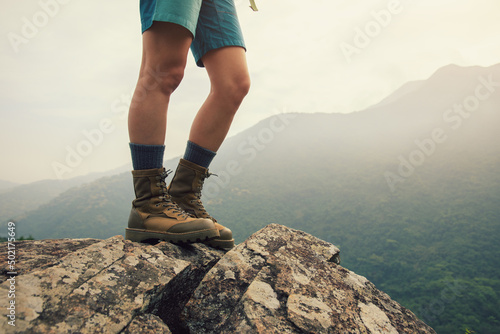 Suceesful woman hiker legs stand on mountain peak cliff edge