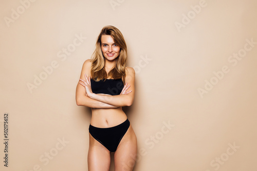 Young woman with perfect body in black underwear standing on beige background