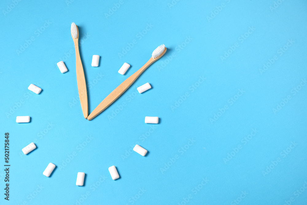 Dental care. Two wooden bamboo eco friendly toothbrushes and chewing gum in the form of hours on blue color background in studio with copy space. Eco friendly and reuse concept. Flat lay, top view Dental care. Two wooden bamboo eco friendly toothbrushes and chewing gum in the form of hours on blue color background in studio with copy space. Eco friendly and reuse concept. Flat lay, top view