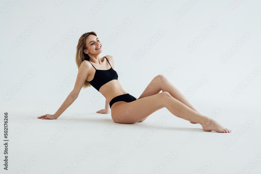 young beautiful woman with perfect body in black underwear sitting on floor on white background