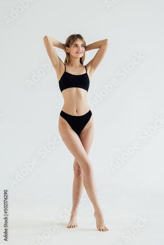 Sporty woman in black bikini posing on grey background. Beauty and body care concept