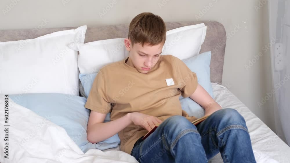 Boy teenager reading book while lying on the bed at home. Slow motion Boy teenager reading book while lying on the bed at home. Slow motion
