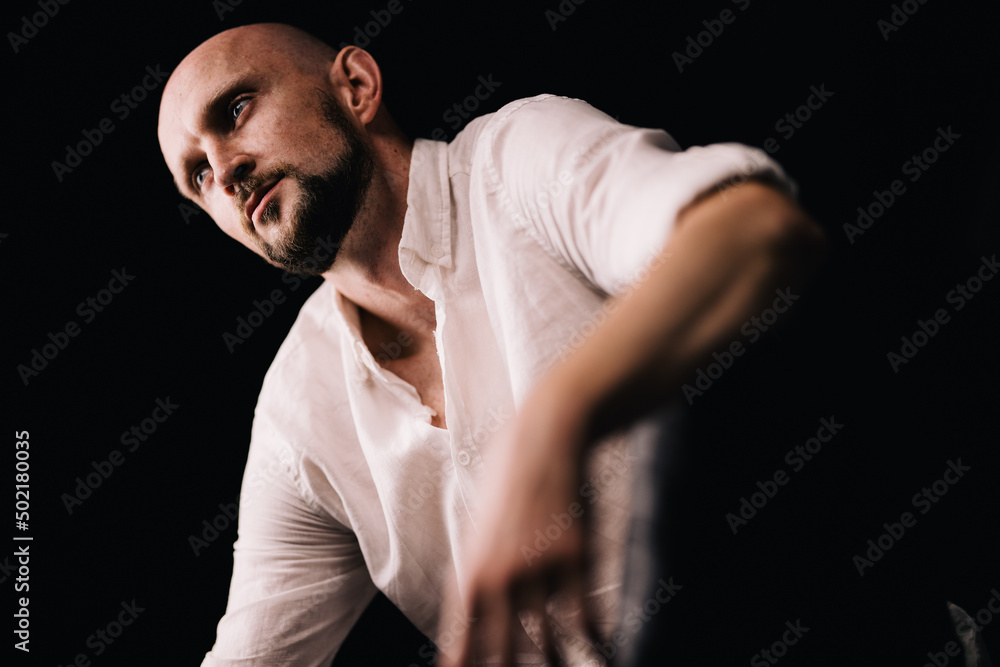 studio portrait of a bald guy with a beautiful beard in a white shirt on a black background