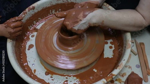 Master teaches apprentice how to make a clay pot on a potter's wheel photo