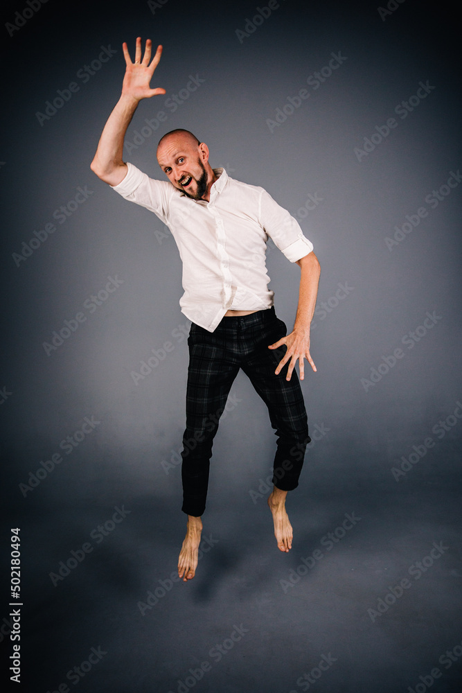 studio portrait of a bald guy with a beautiful beard barefoot in a white shirt and plaid pants dancing on a gray background studio portrait of a bald guy with a beautiful beard barefoot in a white shirt and plaid pants dancing on a gray background