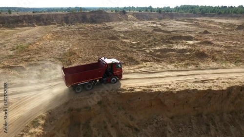 Dump truck driving on rural road. Scene. Top view of truck rides, leaving plumes of dust in dirt road in countryside on background of excavator career © Media Whale Stock