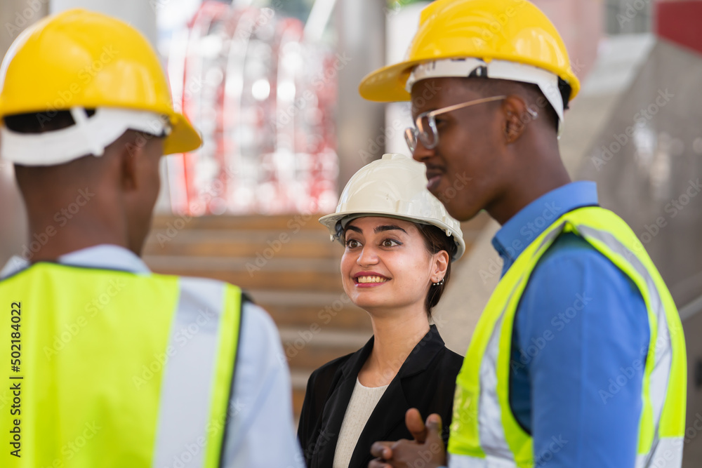 caucasian businesswoman with helmet in black suit happy working with black engineer colleague. group of engineer working at construction site outside building in city caucasian businesswoman with helmet in black suit happy working with black engineer colleague. group of engineer working at construction site outside building in city