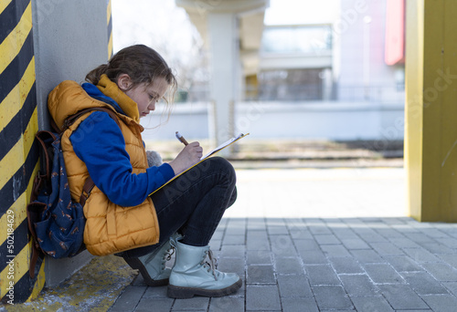 Little Ukrainian child filling form for refugees at train station alone. © Halfpoint