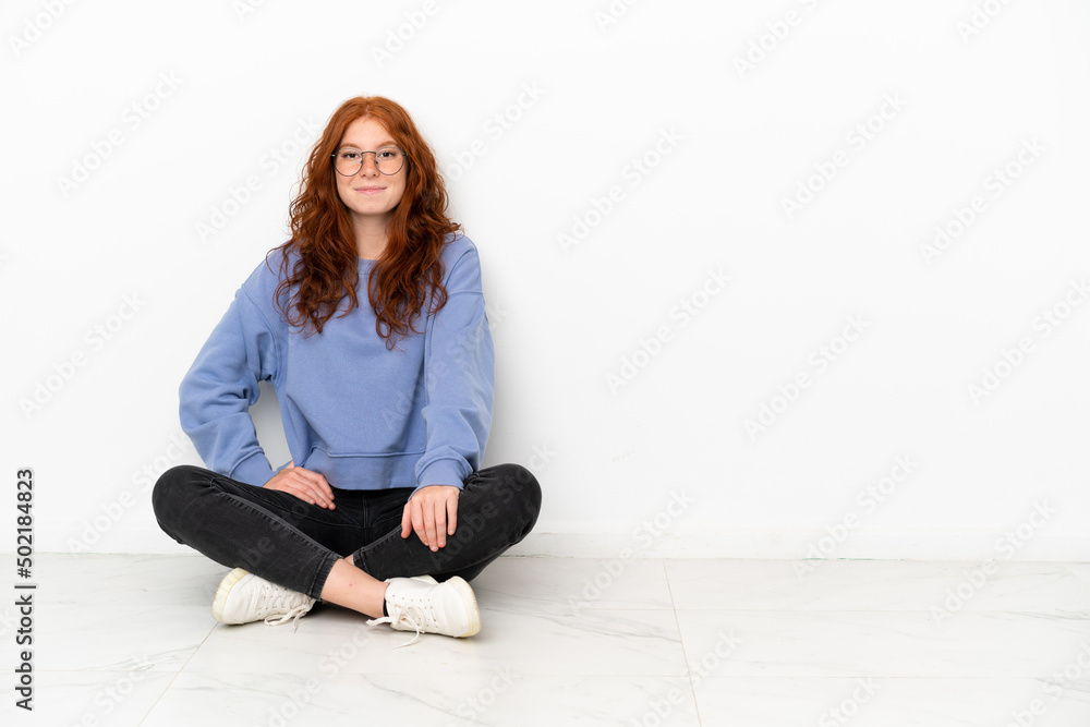 Teenager redhead girl sitting on the floor isolated on white background laughing Teenager redhead girl sitting on the floor isolated on white background laughing