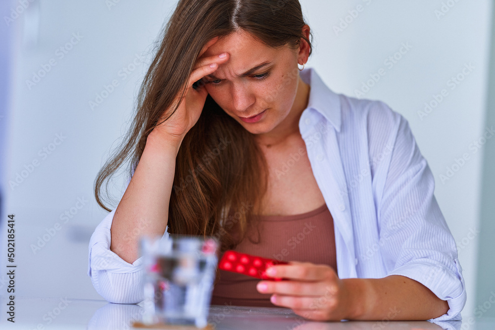 Unhealthy painful woman suffering from headache and holding blister pack with painkiller pills medicine at home. Health problems Unhealthy painful woman suffering from headache and holding blister pack with painkiller pills medicine at home. Health problems