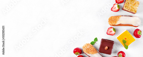 Web banner with cakes assortment. Dessert variation on the white table: Eclairs, mousse cake with passion fruit, with chocolate, pistachio, cheesecake and strawberry. Mockup with copy space