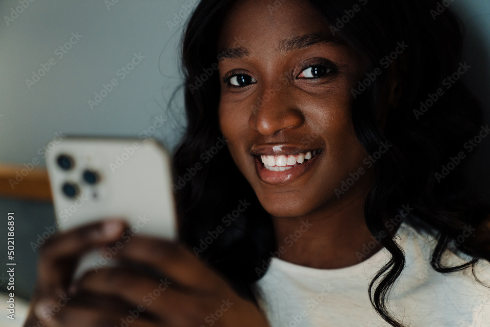 Black woman smiling and using mobile phone while lying in bed at home Black woman smiling and using mobile phone while lying in bed at home