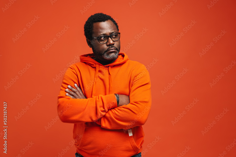 Black sad man in eyeglasses posing with arms crossed - obrazy, fototapety, plakaty 