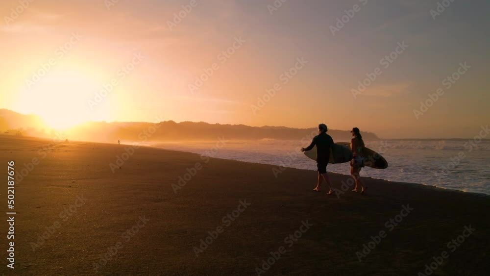 AERIAL SILHOUETTE: Following two surfers walking on the beach carrying surfboards. Surf friends checking waves in golden light before surf session. Gorgeous summer scenery at Playa Venao in Panama. AERIAL SILHOUETTE: Following two surfers walking on the beach carrying surfboards. Surf friends checking waves in golden light before surf session. Gorgeous summer scenery at Playa Venao in Panama.