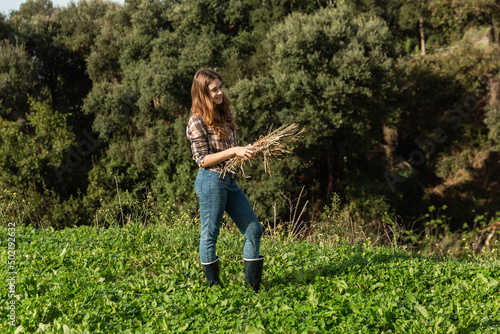 A happy young peasant girl holding hay in a meadow with trees behind her