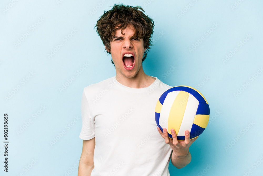 Young caucasian man playing volleyball isolated on blue background screaming very angry and aggressive.
