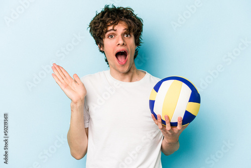 Young caucasian man playing volleyball isolated on blue background surprised and shocked.