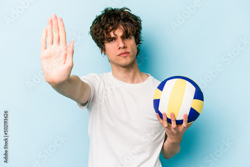 Young caucasian man playing volleyball isolated on blue background standing with outstretched hand showing stop sign, preventing you.