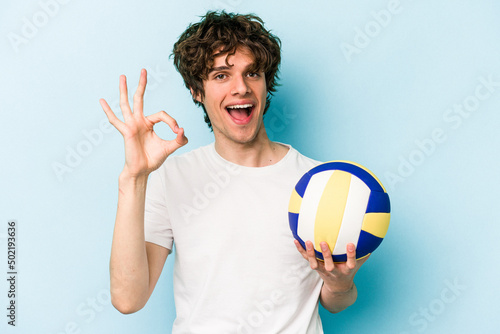 Young caucasian man playing volleyball isolated on blue background cheerful and confident showing ok gesture.