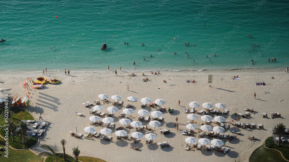 Summer beach with people and turquoise ocean water from top view. Beach on a Sunny day in Dubai view from the top