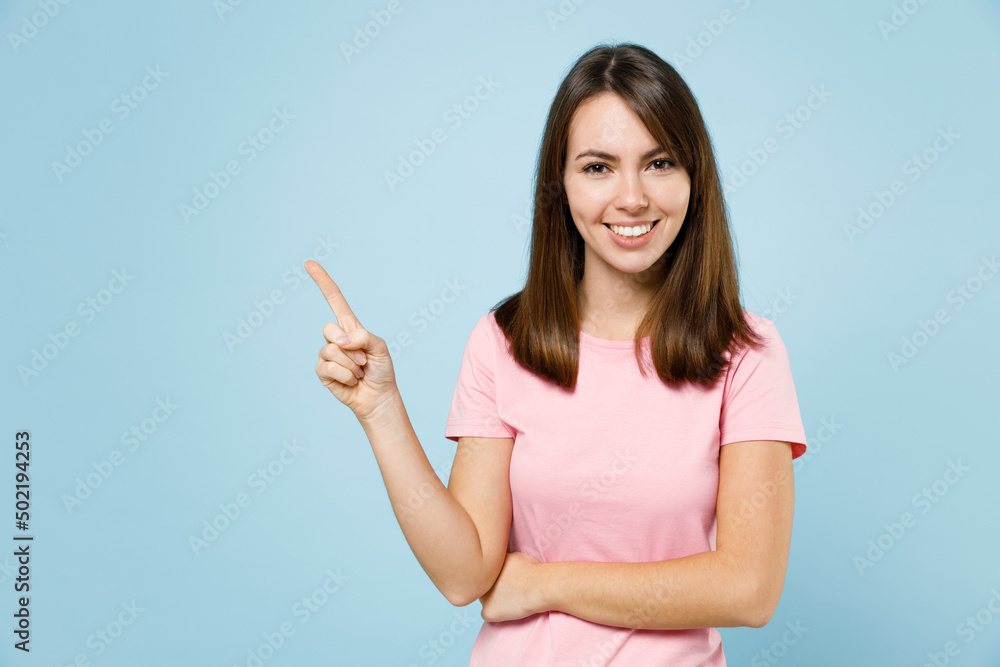 Young smiling happy woman 20s wear pink t-shirt point index finger aside on workspace area mock up copy space isolated on pastel plain light blue background studio portrait. People lifestyle concept. Young smiling happy woman 20s wear pink t-shirt point index finger aside on workspace area mock up copy space isolated on pastel plain light blue background studio portrait. People lifestyle concept.