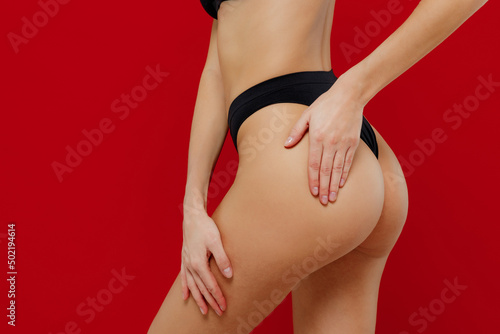 Cropped side view young sexy brunette woman 20s with perfect fit body wear black underwear put hands on buttocks hips without cellulite isolated on plain red background. People female beauty concept