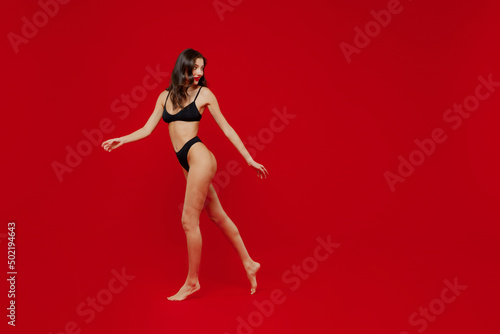Full body side view happy fun young sexy woman 20s with perfect fit body wearing black underwear jump high look aside on workspace area isolated on plain red background. People female beauty concept © ViDi Studio