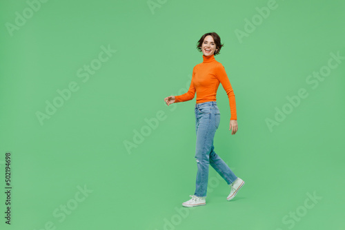 Full body young smiling happy cool fun woman 20s wearing casual orange turtleneck walk going strolling isolated on plain pastel light green color background studio portrait. People lifestyle concept. © ViDi Studio