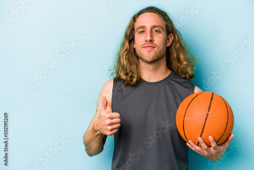 Young caucasian man playing basketball isolated on blue background smiling and raising thumb up