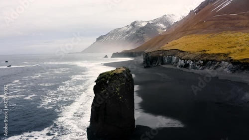 Alone Cliff washed by ocean waves on a black beach in Iceland. Untouched Arctic Nature.