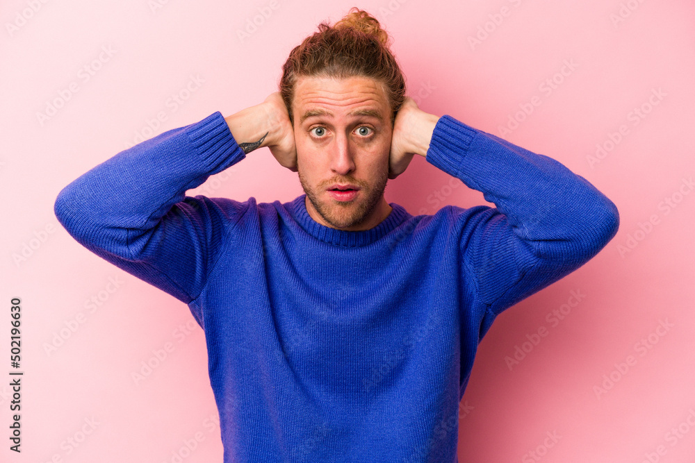 Young caucasian man isolated on pink background covering ears with hands trying not to hear too loud sound. Young caucasian man isolated on pink background covering ears with hands trying not to hear too loud sound.
