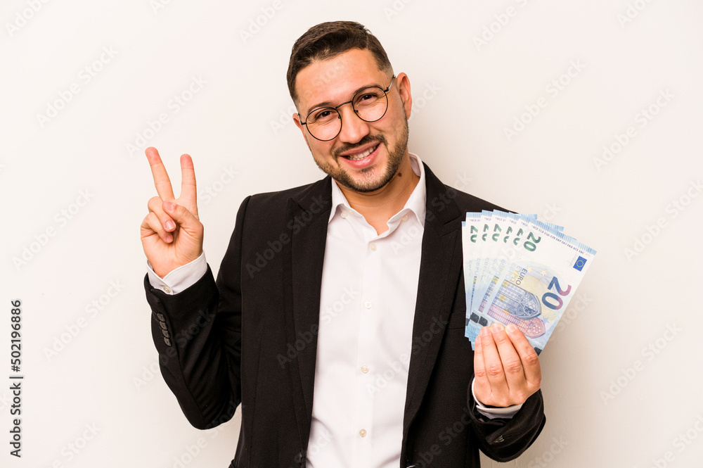 Business hispanic man holding banknotes isolated on white background joyful and carefree showing a peace symbol with fingers. Business hispanic man holding banknotes isolated on white background joyful and carefree showing a peace symbol with fingers.