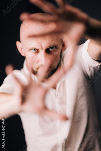 Studio portrait through the fingers of a bald man with a beautiful beard on a black background © Denis