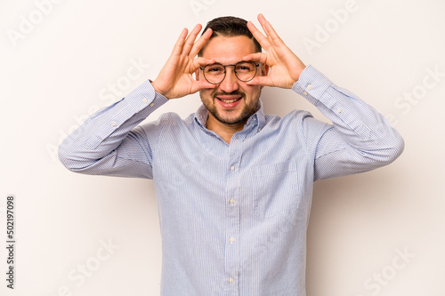 Young hispanic man isolated on white background showing okay sign over eyes