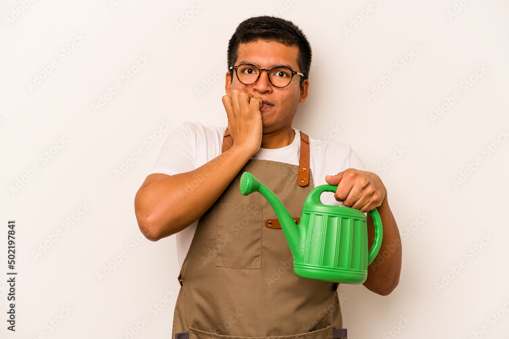 Young gardener hispanic man holding a watering can isolated on white background biting fingernails, nervous and very anxious. Young gardener hispanic man holding a watering can isolated on white background biting fingernails, nervous and very anxious.