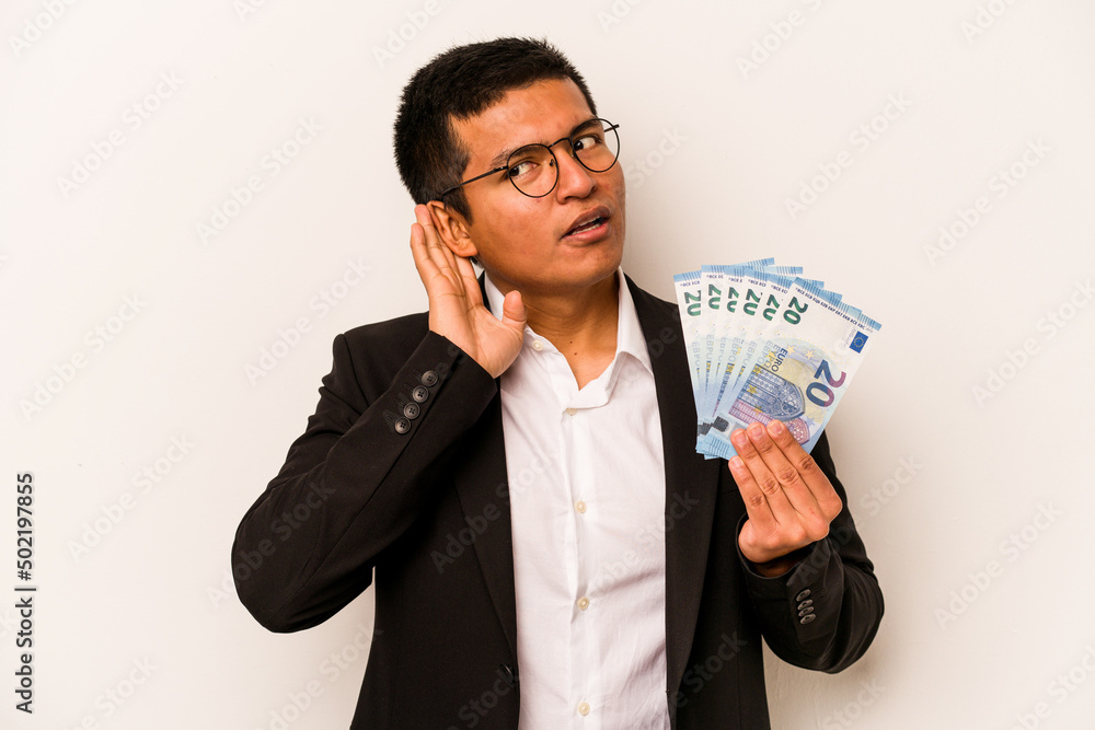 Young hispanic business man holding banknotes isolated on white background trying to listening a gossip. Young hispanic business man holding banknotes isolated on white background trying to listening a gossip.