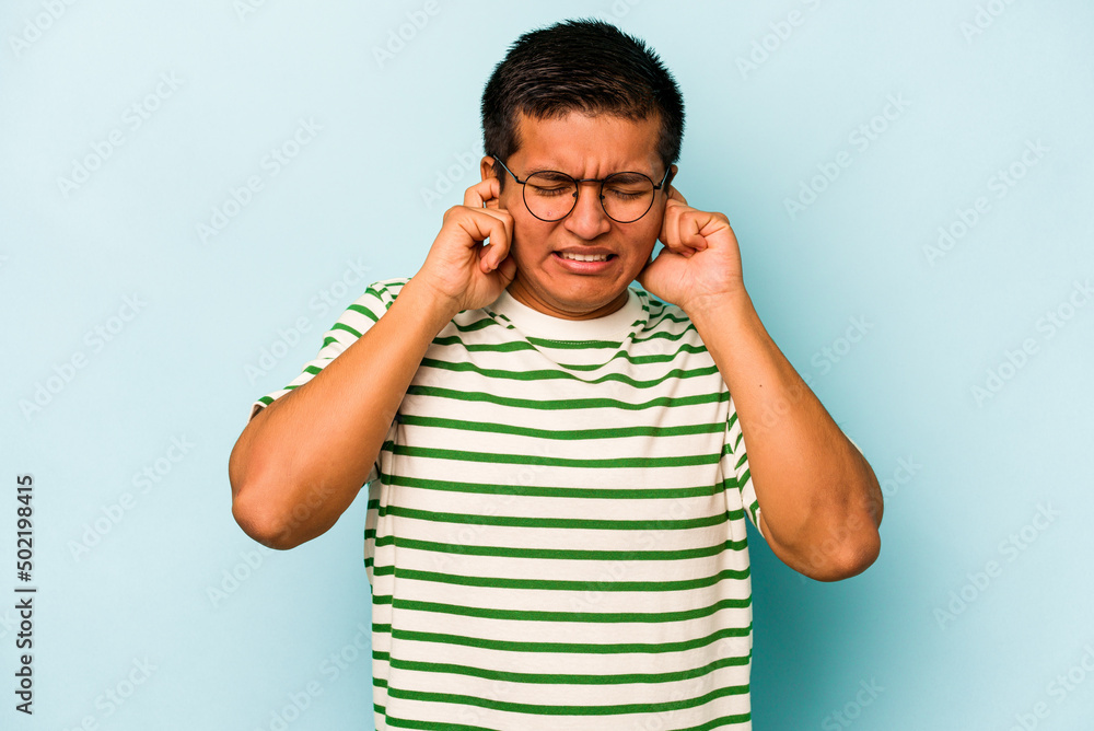 Young hispanic man isolated on blue background covering ears with hands. Young hispanic man isolated on blue background covering ears with hands.