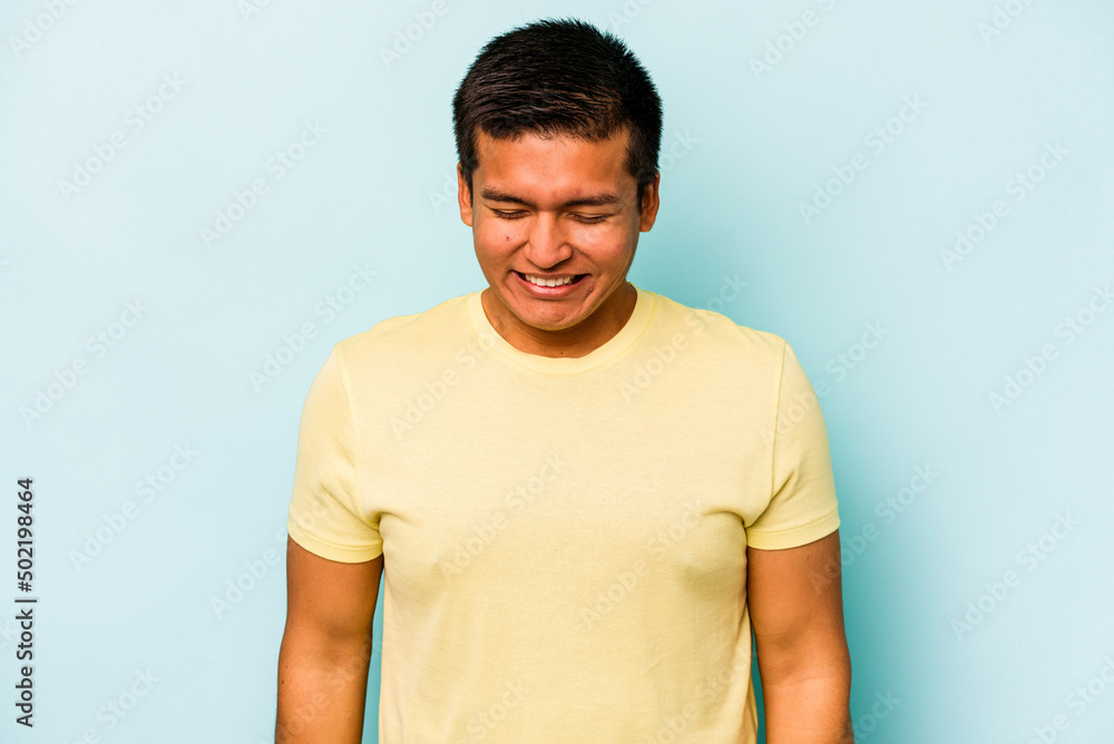 Young hispanic man isolated on blue background laughs and closes eyes, feels relaxed and happy. Young hispanic man isolated on blue background laughs and closes eyes, feels relaxed and happy.
